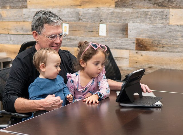 Will Montague at the conference table with two young guests, studying a tablet together