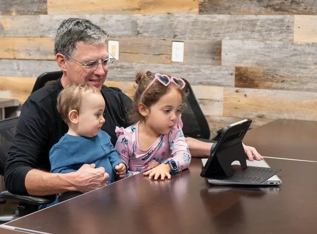 Will Montague at the conference table with two young guests, studying a tablet together